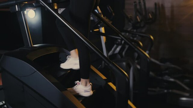 Close-up of the legs of a girl athlete walking on the steps on the exercise machine. Sports step trainer. A girl is training in the gym. Stair climber exercise machine.