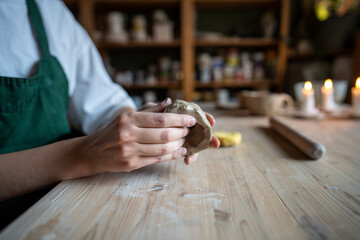 Woman hands sculpting clay at wooden workshop table, creating unique item. Hobby pottery, ceramic shaping, clay art, handmade design, tactile artistry, skilled pottery technique, earthenware produce