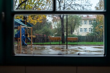 Fototapeta premium The rain blurs the playground as students watch in silence. A gust of wind makes the trees