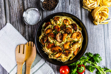 A delicious serving of creamy tagliatelle pasta topped with golden chicken and sautéed mushrooms, garnished with fresh parsley. Presented in a black bowl on a rustic background.