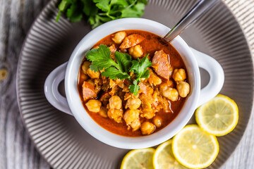 A hearty and flavorful stew featuring tender chickpeas, smoked sausage, and aromatic spices, garnished with fresh cilantro and served with lemon slices for a zesty finish.