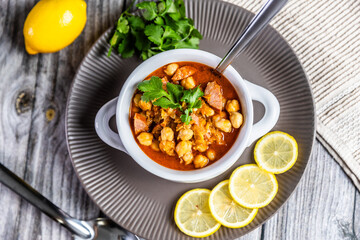 A hearty and flavorful stew featuring tender chickpeas, smoked sausage, and aromatic spices, garnished with fresh cilantro and served with lemon slices for a zesty finish.