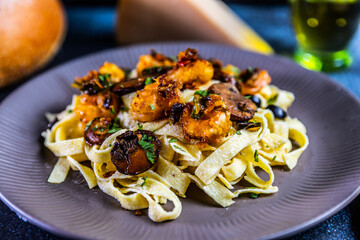 Creamy tagliatelle pasta topped with sautéed shrimp, mushrooms, and black olives, garnished with fresh herbs and Parmesan cheese.