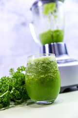 A refreshing glass of green juice prepared in a blender, featuring vibrant green parsley in the background. Perfect for a healthy lifestyle, this natural juice is packed with vitamins and flavor.

