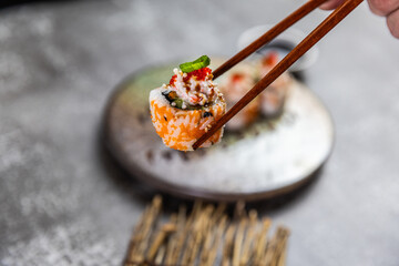 Sushi roll picked with chopsticks on ceramic plate