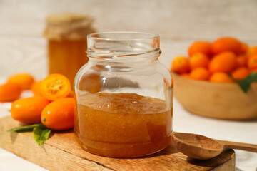 Kumquat and jars of jam on wooden stand on light background, close up
