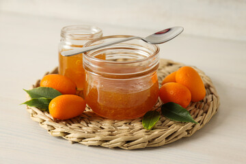 Kumquat and jars of jam on light wooden background