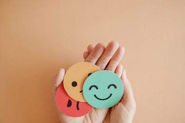 Hands holding sad face hiding behind happy face, bipolar and depression, mental health, split...