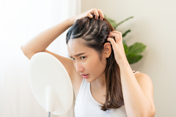Damaged Hair symptom, face serious asian young woman, girl worry about balding, looking at scalp in mirror, hand in break into front hair loss, thin problem. Health care treatment for beauty concept.