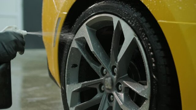 Specialist cleaning a car wheel with spray at a detailing station