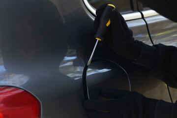 Thief with screwdriver opening fuel cap, closeup. Car hijacking