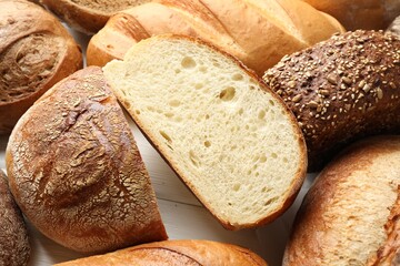 Whole and cut bread loafs on white table, closeup