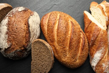 Loafs of different bread on black background, flat lay