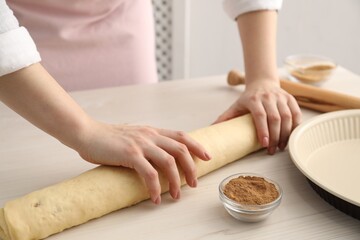 Making cinnamon rolls. Woman shaping dough at white wooden table, closeup