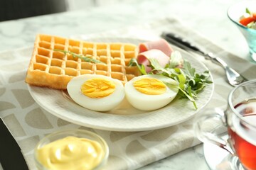 Tasty brunch. Boiled egg, Belgian waffle, arugula, ham and sauce on light table, closeup