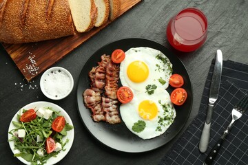 Tasty brunch. Delicious fried eggs, bacon, salad and glass of juice served on black table, flat lay