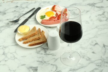 Tasty brunch. Glass of red wine, fried egg, sausage, bread and sauce on white marble table