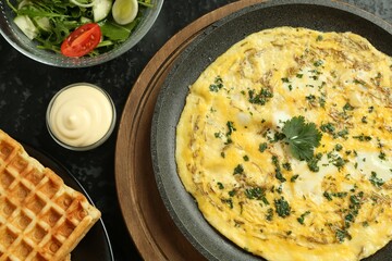 Tasty brunch. Delicious omelette, salad and waffles served on black textured table, flat lay