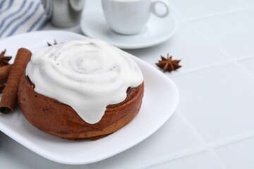 Tasty cinnamon roll with cream and spices on white tiled table, closeup