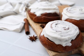 Tasty cinnamon rolls with cream and spices on white tiled table, closeup