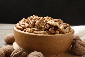 Peeled walnuts in bowl and whole ones on wooden table, closeup