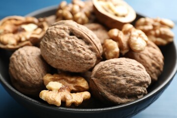 Fresh walnuts in bowl on blue table, closeup