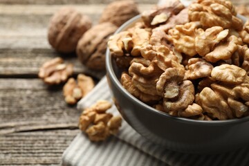Fresh walnuts in bowl on wooden table, closeup. Space for text