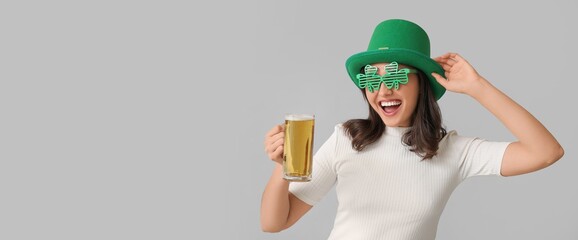Happy young woman in leprechaun hat drinking beer on grey background with space for text. St. Patrick's Day celebration