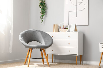 Interior of light living room with cozy grey armchair and chest of drawers