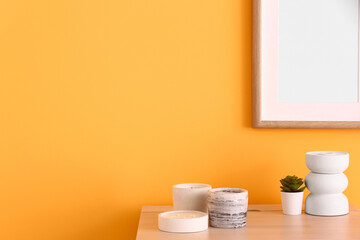 Holders with candles and houseplant near orange wall in room