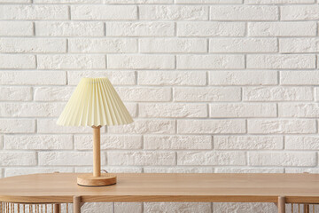 Lamp on wooden table near white brick wall