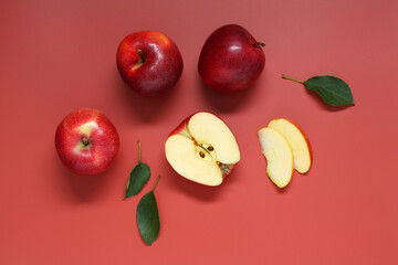 Fresh apples and green leaves on red background, flat lay
