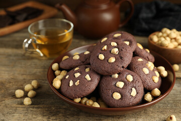 Tasty chocolate cookies with hazelnuts and tea on wooden table, closeup