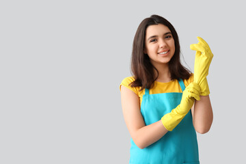 Young woman with rubber gloves on grey background