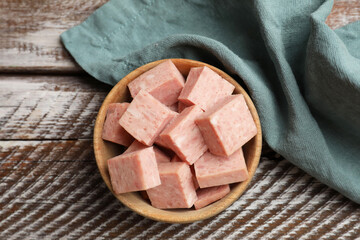 Pieces of canned meat in bowl and towel on wooden table, top view