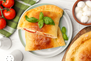 Pieces of tasty vegetarian calzone with tomatoes, mozzarella cheese and basil on white textured table, top view