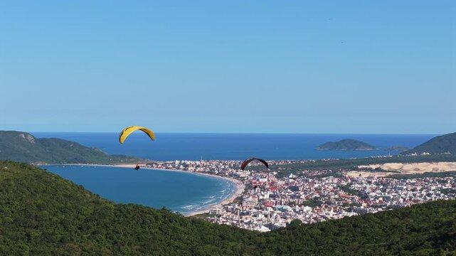 Two paragliders soaring peacefully over a beach in Florian&oacute;polis, Brazil, with a calm and serene atmosphere.