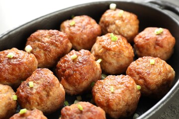 Tasty meatballs with green onion in baking dish on table, closeup