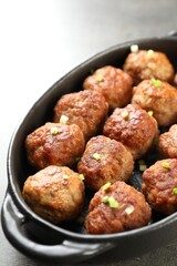 Tasty meatballs with green onion in baking dish on grey table, closeup