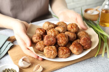 Woman holding plate with delicious meatballs at light textured table, closeup