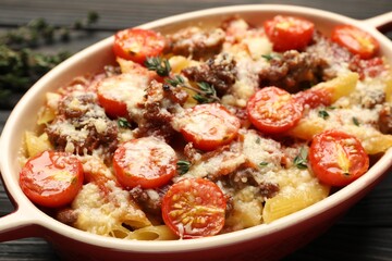 Delicious pasta casserole with cheese, tomatoes, minced meat and thyme in baking dish on table, closeup