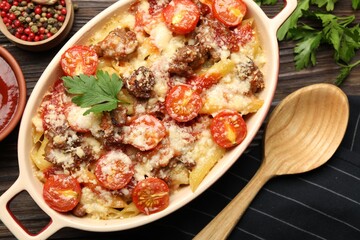 Delicious pasta casserole with cheese, tomatoes and minced meat in baking dish served on wooden table, flat lay