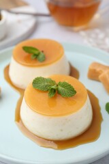 Tasty puddings with caramel sauce served on white table, closeup