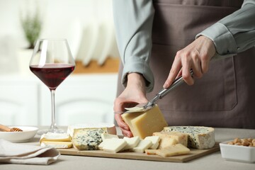 Woman slicing delicious cheese at light textured table indoors, closeup