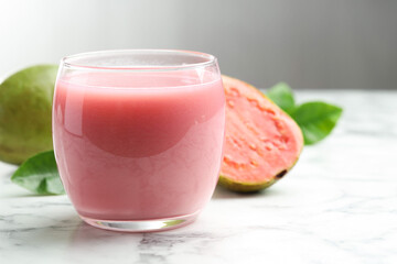 Tasty guava juice in glass, leaves and fruits on white marble table against grey background, closeup