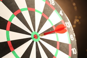 Red arrow hitting target on dart board against black background with blurred lights, closeup