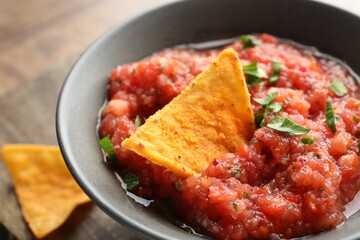 Delicious spicy salsa sauce with nacho chip in bowl on table, closeup