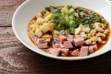 Tasty okroshka soup with kvass in bowl on wooden table, closeup