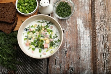 Delicious okroshka soup in bowl on wooden table, flat lay. Space for text