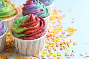 Delicious cupcakes with colorful cream and confetti on light table, closeup. Space for text